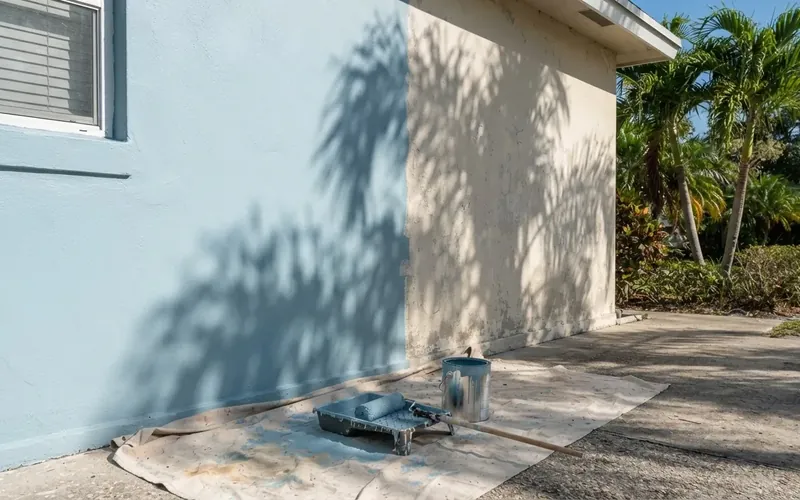 Stucco wall of a Florida home being repainted, with a drop cloth and paint tray